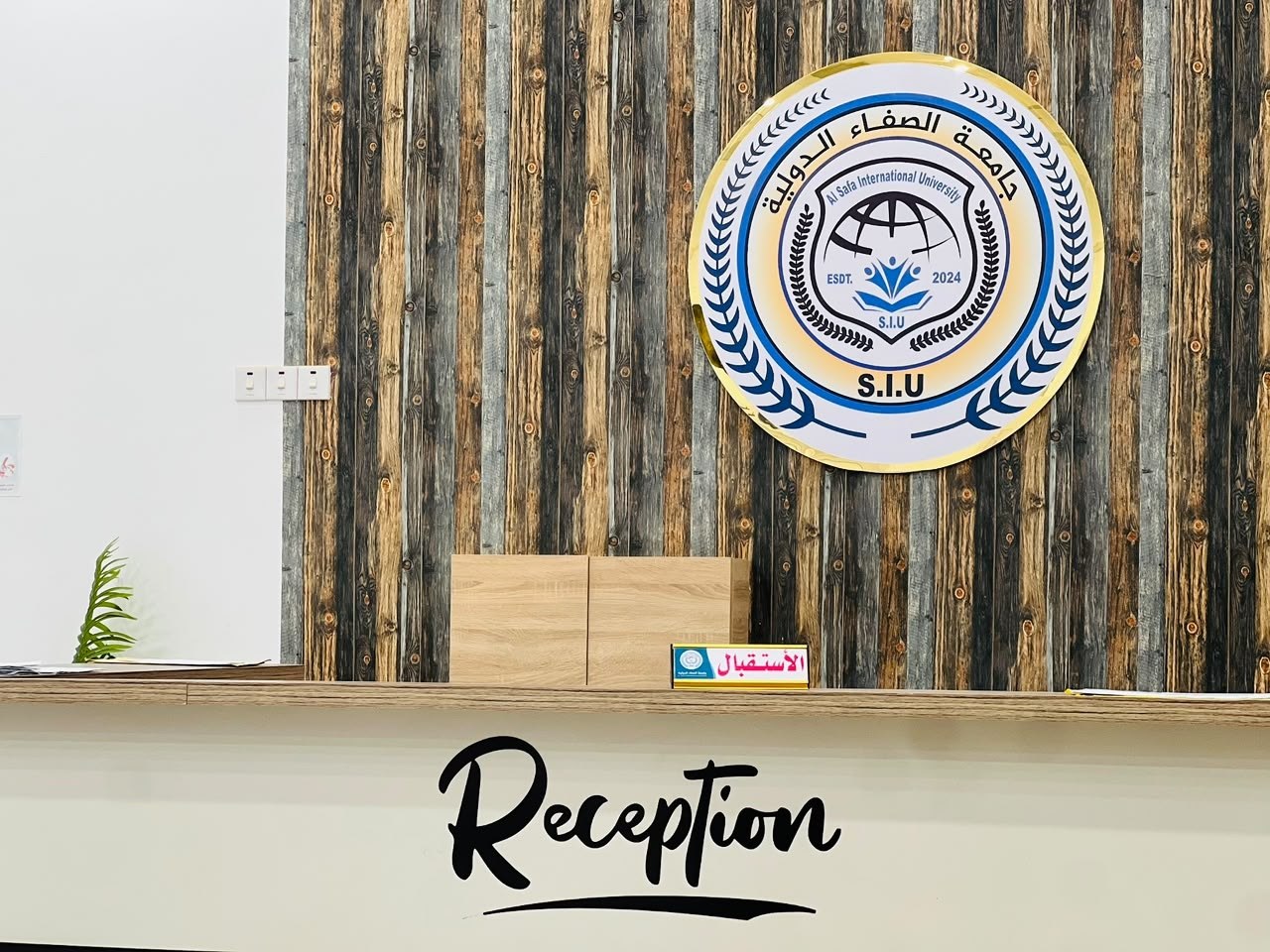 مكتب الاستقبال في جامعة الصفاء الدولية بطبرق وشعار الجامعة معلّق على الجدار الخشبي